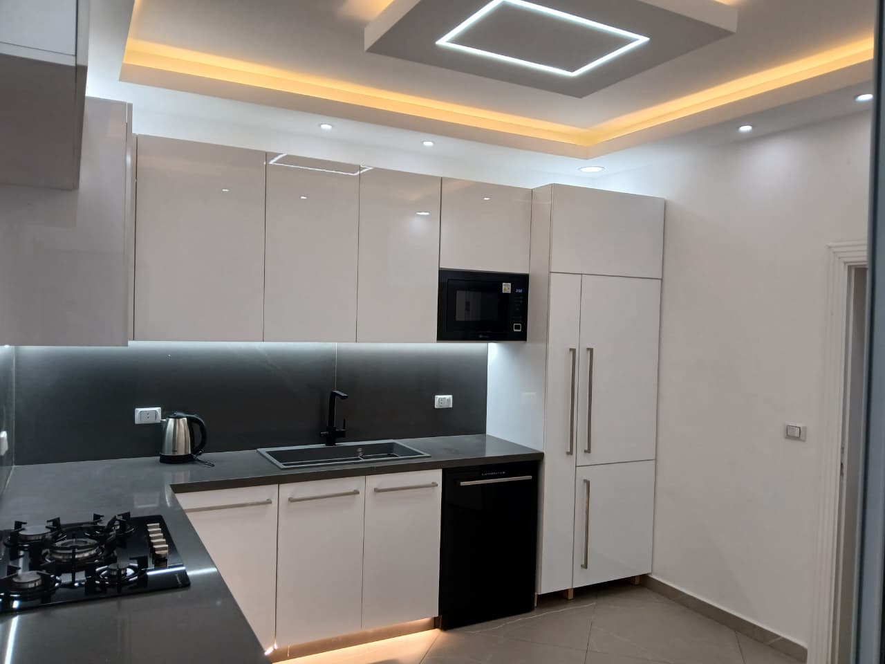 Modern kitchen with glossy white cabinets, dark counters and ambient LED lighting